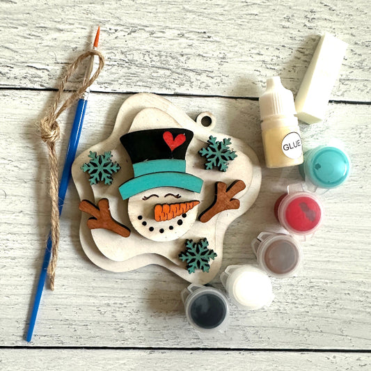 Decorative snowman ornament with paint supplies on a wooden surface