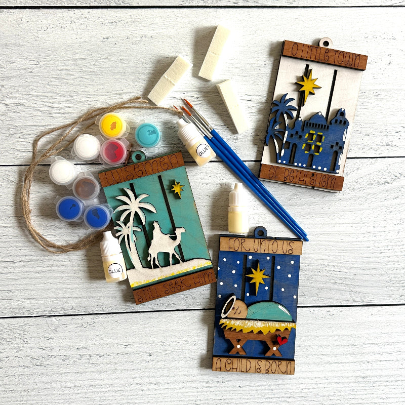 Decorative nativity ornaments with paint supplies on a wooden surface