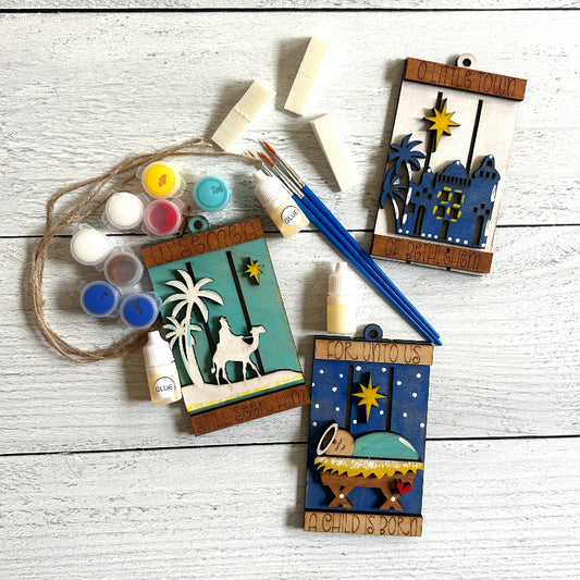 Decorative nativity ornaments with paint supplies on a wooden surface