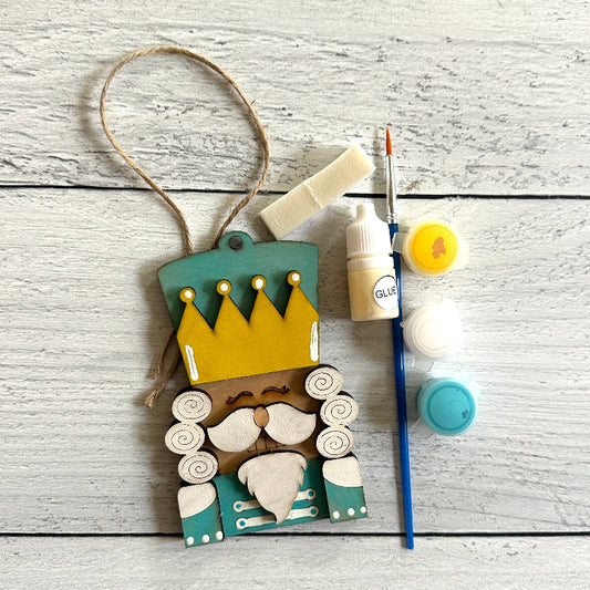 Decorative wooden nutcracker ornament with a crown, glue, paint, and brush on a wooden surface