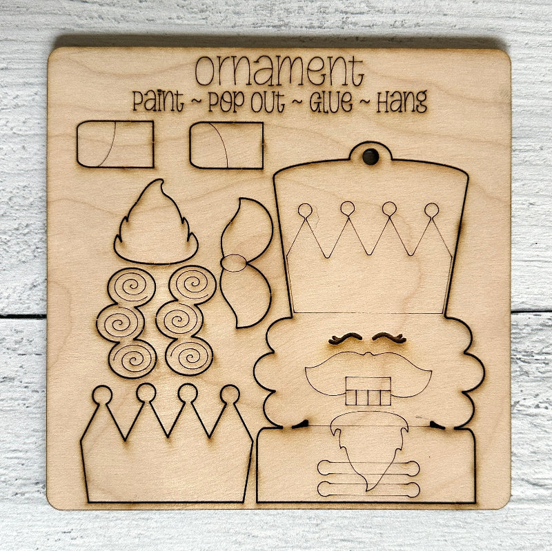 Wooden cutout with laser-engraved nutcracker design elements for a Christmas ornament on a light wooden surface.
